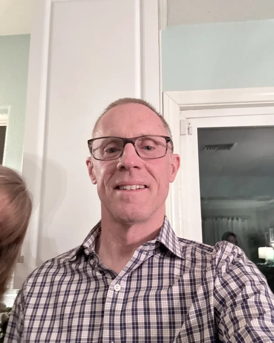 Courtland Keith, D.C., indoors, wearing glasses and a black-and-white checkered button-down.