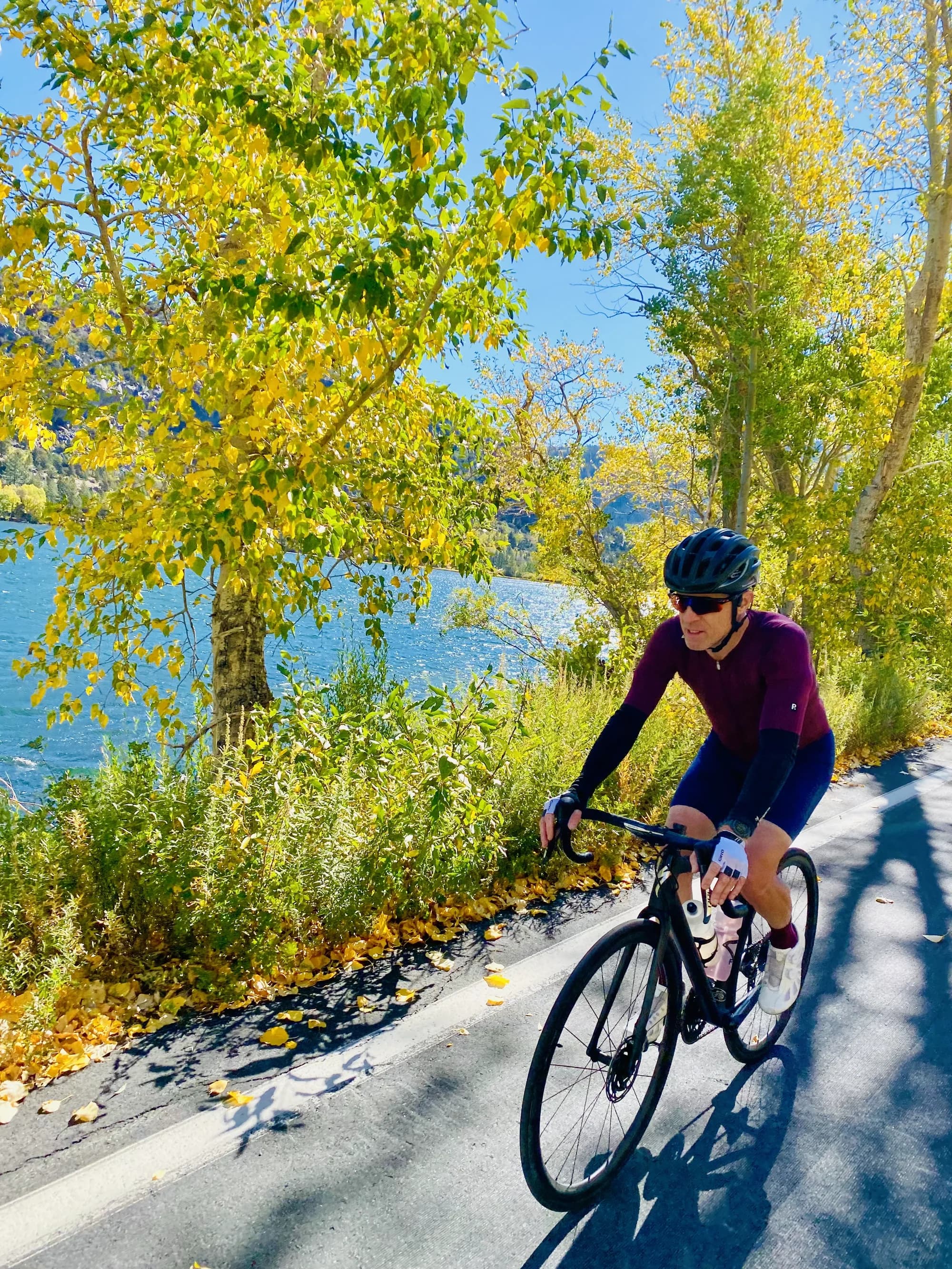Courtland Keith riding a road bike beside a lake, with autumn trees along the road.
