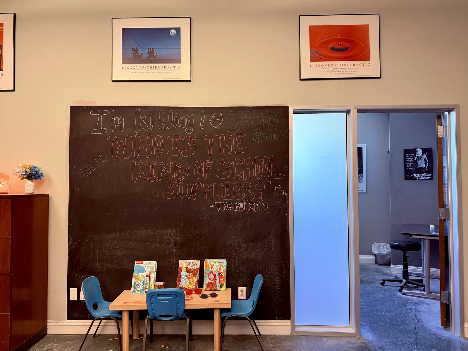 Kids’ corner of the office with a chalkboard drawing, a wooden toy box, children’s books, and a small table. No people are shown.